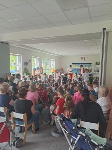 Dzieci oraz panie oglądające teatrzyk. Naprzeciw stoi dwóch mężczyzn występujących w teatrzyku.