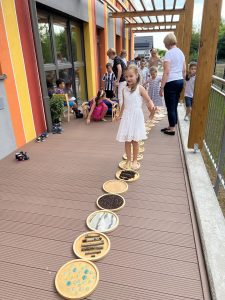 Dzieci stoją w rzędzie, przechodzą kolejno po ścieżce sensorycznej.