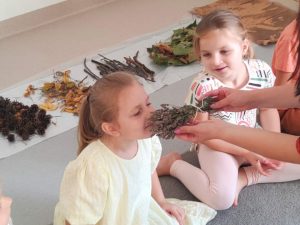 Dziewczynka w białej bluzce wącha lawendę, którą trzyma pani.