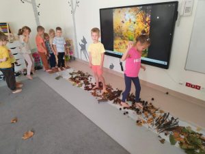 Dziewczynka i chłopiec na bosaka chodzą po ścieżce ułożonej z elementów jesieni (kasztany, żołędzie, liście).