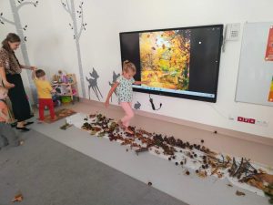 Dziewczynka na bosaka chodzi po ścieżce ułożonej z elementów jesieni (kasztany, żołędzie, liście).