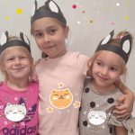 Trzy dziewczynki stoją obok siebie, przytulają się i są uśmiechnięte. Na głowie mają uszy kocie.