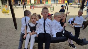 Grupka dzieci siedzi na czarnej huśtawce i się bujają.