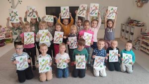 Grupa dzieci stoi w trzech rzędach i trzyma prace plastyczne - kolorowe trąbki.