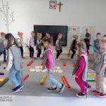 Dzieci w strojach kotów maszerują w takt muzyki dookoła dywanu.
