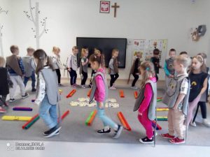 Dzieci w strojach kotów maszerują w takt muzyki dookoła dywanu.