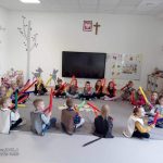 Dzieci siedzą na szarym dywanie i grają na kolorowych ,, bum bum rurkach".