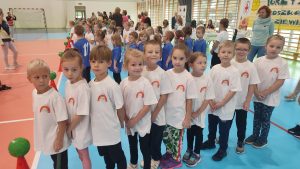 10 dzieci w białych koszulkach stoją w rzędzie i czekają na swoją kolej w zawodach sportowych.
