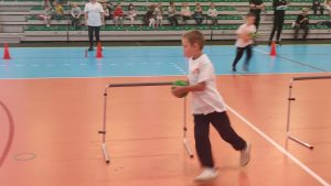 Chłopiec biegnie z zieloną piłką na około bramki.