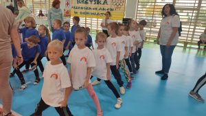 10 dzieci w białych koszulkach stoją w rzędzie i czekają na swoją kolej w zawodach sportowych.