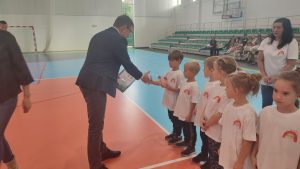 Mężczyzna wręcza grupie dzieci dyplom uczestnictwa w zawodach sportowych.