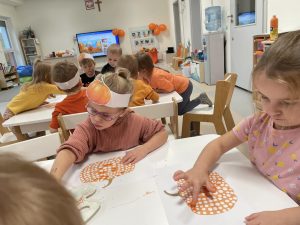 Dzieci przy stolikach ozdabiają farbą dynie