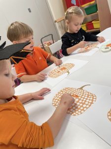 Dzieci przy stolikach ozdabiają farbą dynie