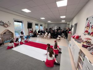 Dziewczynki siedzą wzdłuż flagi biało-czerwonej. W tyle siedzą pozostałe dzieci.