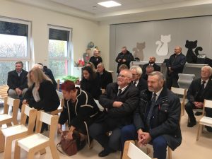 Zaproszeni goście ubrani na czarno siedzą na krzesłach.