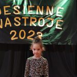 Dziewczynka w czarnej spódniczce i bluzce w brązowe ciapki stoi na scenie MDK i pozuje do zdjęć.