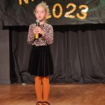 Dziewczynka w czarnej spódniczce i bluzce w brązowe ciapki stoi na scenie MDK i wykonuje piosenkę ,, Jesienna poleczka".