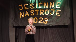 Dziewczynka w czarnej spódniczce i bluzce w brązowe ciapki stoi na scenie MDK i wykonuje piosenkę ,, Jesienna poleczka".