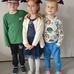 Jedna dziewczynka i dwóch chłopców ubranych na pomarańczowo pozują do zdjęć z symbolami Halloween.
