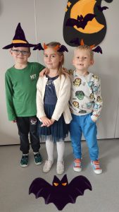 Jedna dziewczynka i dwóch chłopców ubranych na pomarańczowo pozują do zdjęć z symbolami Halloween.