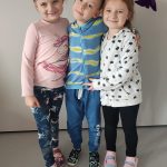 Jeden chłopiec i dwie dziewczynki ubranych na kolorowo pozują do zdjęć z symbolami Halloween.