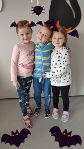 Jeden chłopiec i dwie dziewczynki ubranych na kolorowo pozują do zdjęć z symbolami Halloween.
