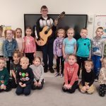 DZieci pozują wspólnie do zdjęcia z chłopcem, który trzyma gitarę.