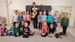 DZieci pozują wspólnie do zdjęcia z chłopcem, który trzyma gitarę.