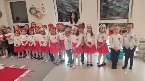 Grupa dzieci w strojach narodowych stoją obok siebie i śpiewają hymn narodowy.