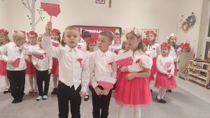 Dzieci w strojach narodowych tańczą i śpiewają w sali.