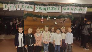 8 dzieci w strojach odświętnych stoi na tle brązowej ściany z napisem Ekologia, świąteczne marzenia. Dzieci pozują do zdjęć.