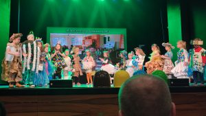 Grupa dzieci na scenie ubrani w stroje ekologiczne wykonane z odpadów pozuje do zdjęć.