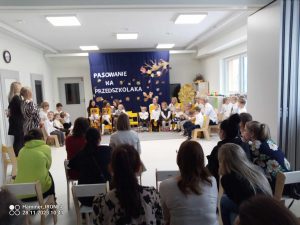 Rodzice siedzą na krzesełkach i oglądają dzieci , które występują.