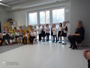 Dzieci ubrani na galowo stoją obok siebie i recytują wiersze i śpiewają piosenkę na uroczystości.