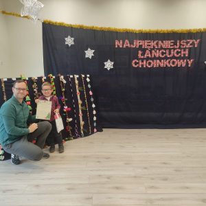 CHŁOPIEC POZUJE DO ZDJĘCIA Z TATĄ NA TLE SWOJEJ PRACY KONKURSOWEJ