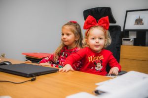 Dwie dziewczynki siedzące we fotelu przy biurku. Przed dziećmi na biurku znajduje się laptop.