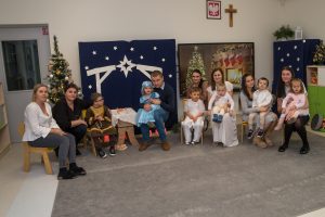Na zdjęciu, na tle dekoracji Bożonarodzeniowej rodzice z dziećmi. Zdjęcie pamiątkowe.