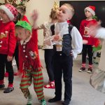 Grupa dzieci w strojach świątecznych wykonuje figury do muzyki. Tańczą.