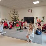Grupa dzieci w strojach świątecznych wykonuje figury do muzyki. Tańczą.