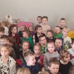 Grupa dzieci siedzi na kolanach na szarym dywanie i patrzy na pana Górnika.