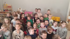 Grupa dzieci siedzi na kolanach na szarym dywanie i patrzy na pana Górnika.