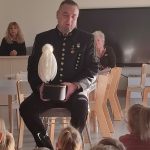 Mężczyzna w stroju górnika siedzi na białym krześle przed grupą dzieci.
