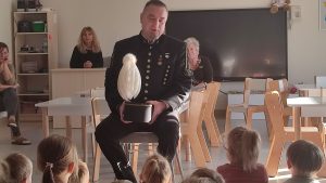 Mężczyzna w stroju górnika siedzi na białym krześle przed grupą dzieci.