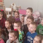 Grupa dzieci siedzi na kolanach na szarym dywanie i patrzy na pana Górnika.
