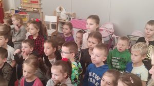 Grupa dzieci siedzi na kolanach na szarym dywanie i patrzy na pana Górnika.