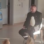 Mężczyzna w stroju górnika siedzi na białym krześle przed grupą dzieci.