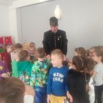Grupa dzieci otacza mężczyznę w stroju górnika. Dzieci rozmawiają i podają rękę górnikowi.