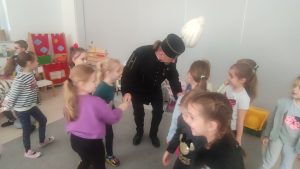 Grupa dzieci otacza mężczyznę w stroju górnika. Dzieci rozmawiają i podają rękę górnikowi.