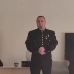 Mężczyzna w stroju górnika stoi na tle szarej ściany przed grupą dzieci.