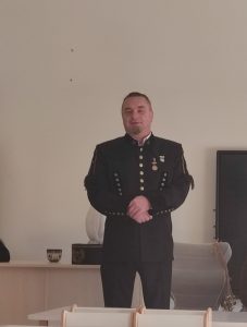 Mężczyzna w stroju górnika stoi na tle szarej ściany przed grupą dzieci.
